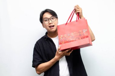 Beyaz arka planda izole edilmiş Kırmızı Batik desenli alışveriş çantası taşıyan çekici ve şık Asyalı genç adam. 