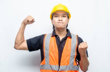 Asyalı inşaat işçisi, sarı sapkalı ve turuncu yelekli ve kaslı. Gücünü ve gücünü göstermek için. Güçlü İşçi Konsepti.