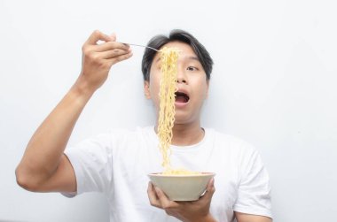 Genç yakışıklı Asyalı adam kaseden erişte çorbası içiyor ve çatal kullanarak büyütüyor. 