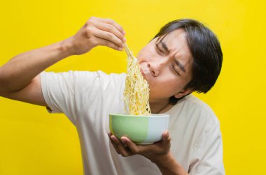 Günlük tişörtlü genç Asyalı Adam Aç İfadesiyle Yemek Yiyen ve Yutan Şehriye Çubuklarını Kullanıyor