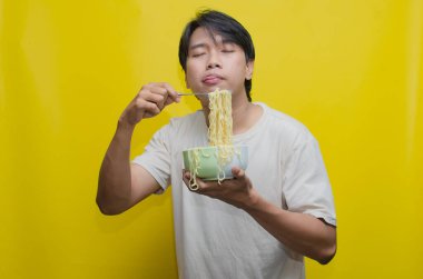 Asyalı Adam, onları çatalla kaldırarak bir kasede erişte yiyor. Krem rengi krem rengi tişörtlü genç Asyalı Çatallı Lezzetli Erişte Çorbası