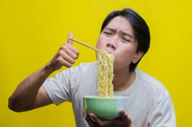 Günlük tişörtlü genç Asyalı Adam Aç İfadesiyle Yemek Yiyen ve Yutan Şehriye Çubuklarını Kullanıyor