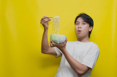 Asyalı Adam, onları çatalla kaldırarak bir kasede erişte yiyor. Krem rengi krem rengi tişörtlü genç Asyalı Çatallı Lezzetli Erişte Çorbası