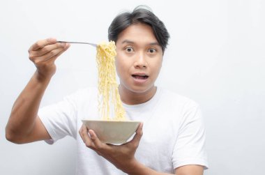 Genç yakışıklı Asyalı adam kaseden erişte çorbası içiyor ve çatal kullanarak büyütüyor. 