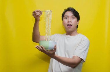 Asyalı Adam, onları çatalla kaldırarak bir kasede erişte yiyor. Krem rengi krem rengi tişörtlü genç Asyalı Çatallı Lezzetli Erişte Çorbası