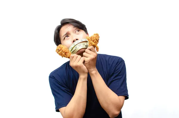 Anoreksi Yeme Bozukluğu. Mutsuz Asyalı Genç Adam Ağzı Ölçüm Bantlı Üzgün Bakışlı Kızarmış Tavuk. Diyet yapan Asyalı Adam Ölçüm Bantını kullanarak Ağzını Örtüyor.