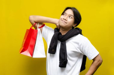 Alışveriş torbaları tutan düşünceli genç Asyalı adam, alışverişlerini düşünüyor. Alışveriş, karar verme ya da tüketici davranışı kavramları için ideal