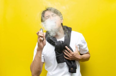 Young Asian man holding his chest in pain while smoking or vaping, with smoke rising. Depicts the health risks of smoking, including chest pain, respiratory issues, and long-term damage clipart