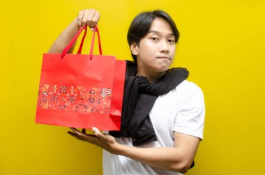 Alışveriş torbaları taşıyan mutlu ve şaşırmış genç Asyalı adam alışverişler konusunda heyecanını dile getiriyor. Perakende, satış ve tatil alışverişi için mükemmel.