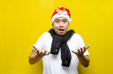 Sarı arka planda Noel Baba şapkası takan Asyalı genç adam şaşırdı. 