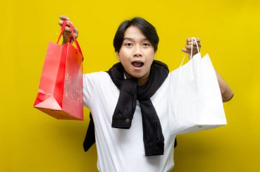 Alışveriş torbaları taşıyan mutlu ve şaşırmış genç Asyalı adam alışverişler konusunda heyecanını dile getiriyor. Perakende, satış ve tatil alışverişi için mükemmel.