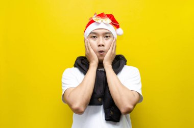 Sarı arka planda Noel Baba şapkası takan Asyalı genç adam şaşırdı. 