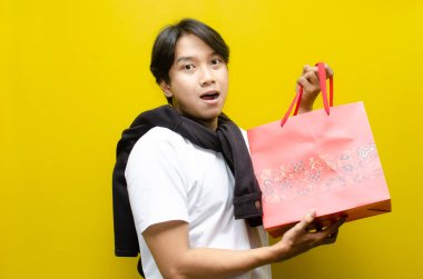 Alışveriş torbaları taşıyan mutlu ve şaşırmış genç Asyalı adam alışverişler konusunda heyecanını dile getiriyor. Perakende, satış ve tatil alışverişi için mükemmel.