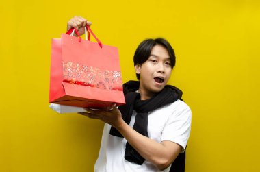 Alışveriş torbaları taşıyan mutlu ve şaşırmış genç Asyalı adam alışverişler konusunda heyecanını dile getiriyor. Perakende, satış ve tatil alışverişi için mükemmel.