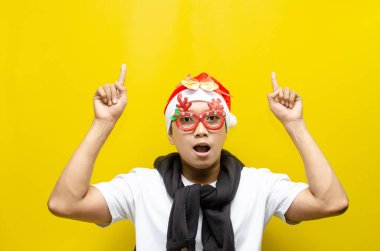 Asyalı genç adam kırmızı Noel Baba şapkası ve komik gözlükler takıyor sarı arka plan, noel konsepti, fotokopi alanı 