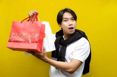 Alışveriş torbaları taşıyan mutlu ve şaşırmış genç Asyalı adam alışverişler konusunda heyecanını dile getiriyor. Perakende, satış ve tatil alışverişi için mükemmel.
