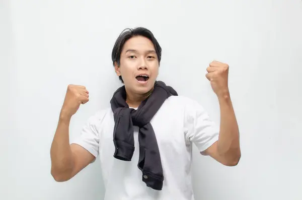 Neşeli bir zaferi kutlamak için sıradan kıyafetler içindeki heyecanlı ve şaşırmış Asyalı genç adam. Başarı, mutluluk ve başarı kavramları için mükemmel.