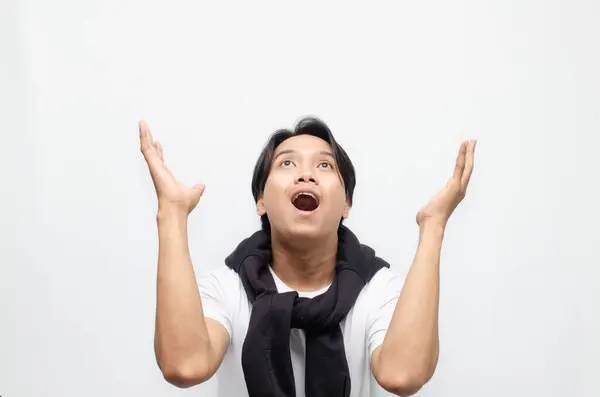 Neşeli bir zaferi kutlamak için sıradan kıyafetler içindeki heyecanlı ve şaşırmış Asyalı genç adam. Başarı, mutluluk ve başarı kavramları için mükemmel.