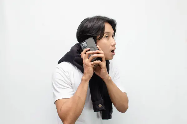 Neşeli ve şaşırmış bir ifadeyle elinde akıllı telefon tutan sıradan giyinmiş heyecanlı Asyalı genç bir adam. Teknoloji, mutluluk veya olumlu tepkiler için mükemmel bir tema.