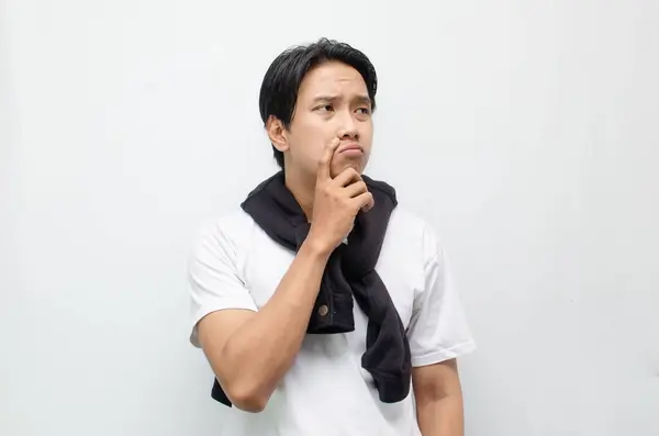 Beyaz tişörtlü Asyalı adam üzgün görünmeyi düşünüyor. 