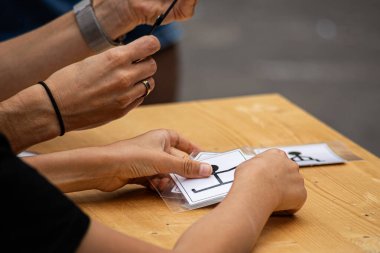 Bir kişi elindeki bir deste kartı dikkatle tutarak elindeki işe odaklanıyor. Görüntü bir konsantrasyon ve hassasiyet anı yakalıyor, öğrenme, oyun ve diğer aktivitelerde ellerin ve detayların kullanımını vurguluyor.