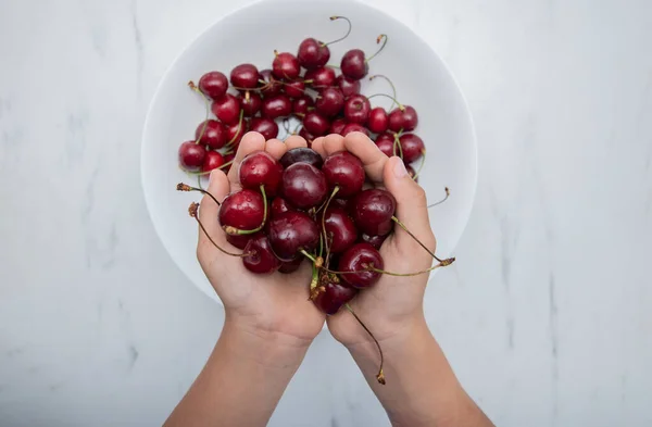 Bir çocuğun elindeki kirazlar beyaz bir tabağa karşı..