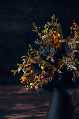 Black metal vase with flowers on a brown  background and a wooden surface