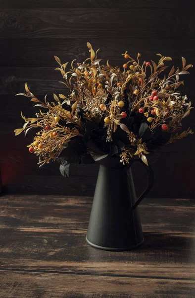 Black metal vase with flowers on a brown  background and a wooden surface