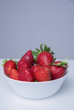 Beyaz bir tabakta taze çilekler, beyaz bir arka planda.