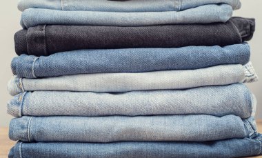 Ahşap masa üzerinde farklı kot pantolon yığını. Gri arka plan. yakın plan