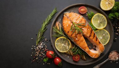 Siyah arka planda ızgara somon bifteği ve limon ve şifalı bitkiler.