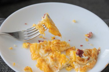 Beyaz tabak ve çatallı jambonlu omlet.