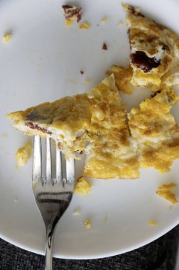 Beyaz tabak ve çatallı jambonlu omlet.