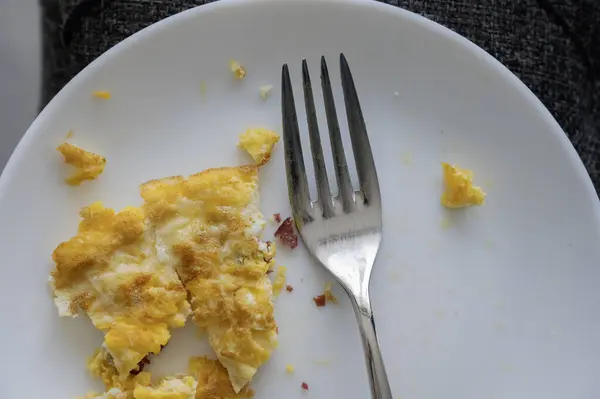 Beyaz tabak ve çatallı jambonlu omlet.