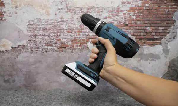 stock image Electric turquoise power drill in hand against a brick wall.