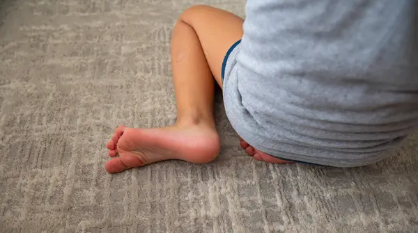 Çocuk kucağında yerde oturuyor, ayaklar halıya yakın. Otizm konsepti.,