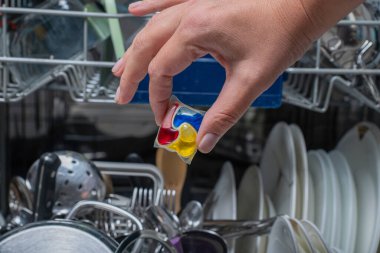 Kadın deterjan kapsülünü açık bulaşık makinesine koyuyor..