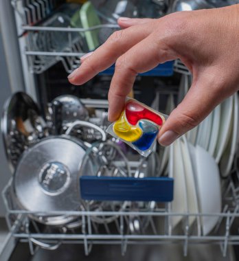 Kadın deterjan kapsülünü açık bulaşık makinesine koyuyor..