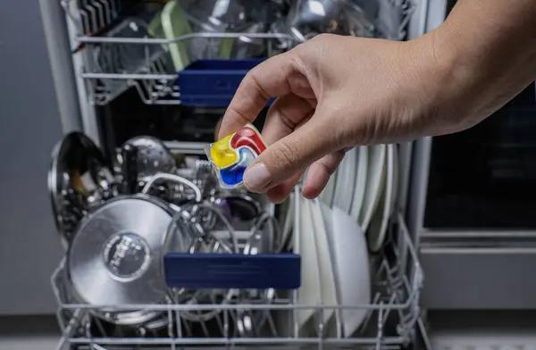 Kadın deterjan kapsülünü açık bulaşık makinesine koyuyor..