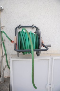 Bahçeyi sulamak için duvarda asılı yeşil renkli hortum..