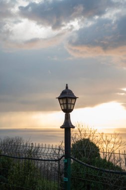 Sütunun üstündeki bahçe lambası. Gün batımının arka planında güzel parlak bir lamba.