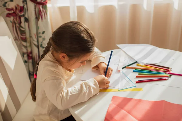 child girl painting with colored pencils and making crafts and cardboard and colored paper uses glue and scissors