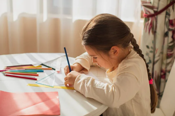 child girl painting with colored pencils and making crafts and cardboard and colored paper uses glue and scissors
