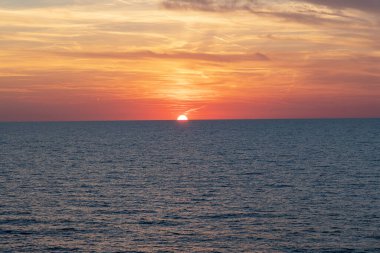 Bir geminin güvertesinden çekilen açık deniz üzerinde nefes kesici bir günbatımı görüntüsü. Huzurlu ufuk ve sıcak gökyüzü renkleri huzurlu ve resim gibi bir an yaratır..