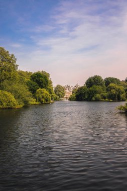 Londra 'daki St. Jamess Park Gölü' nün sakin bir manzarası. Yeşillik ve arka plandaki ikonik At Muhafızları binası çerçeveli. Huzurlu ortam, Londra 'nın en güzel kraliyet parklarından birindeki doğa ve mimarinin uyumunu yansıtıyor.