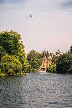 Londra 'daki St. Jamess Park Gölü' nün sakin bir manzarası. Yeşillik ve arka plandaki ikonik At Muhafızları binası çerçeveli. Huzurlu ortam, Londra 'nın en güzel kraliyet parklarından birindeki doğa ve mimarinin uyumunu yansıtıyor.