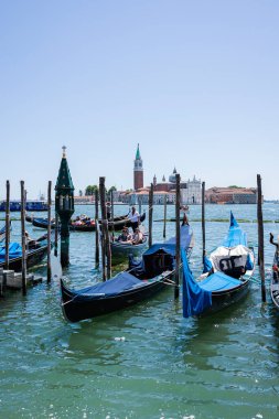 İtalya, Venedik 'teki San Giorgio Maggiore adasının sakin bir manzarası. İkonik kilise ve çan kulesi açık mavi gökyüzüne karşı yükseliyor. Venedik Gölünün sakin sularında ilerleyen bir motorlu tekne ön planda.