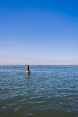 Berrak mavi gökyüzünün altındaki Venedik Gölünün sakin manzarası, huzurlu suları ve geleneksel yön bulma işaretini gösteriyor..