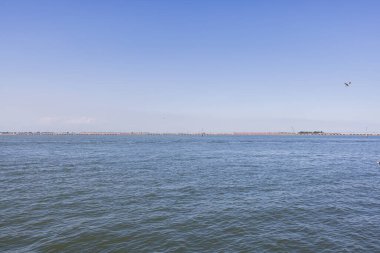 Berrak mavi gökyüzünün altındaki Venedik Gölünün sakin manzarası, huzurlu suları ve geleneksel yön bulma işaretini gösteriyor..