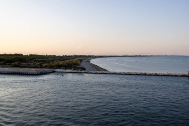 Venedik suları üzerinde nefes kesici bir günbatımı, bir deniz feneri ve kıyı şeridinin siluetini aydınlatıyor. Altın renkler dalgalanan dalgalara güzelce yansıyor.